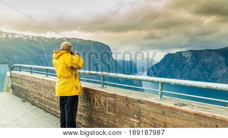 Tourism and travel. Male tourist nature photographer taking photo with camera enjoying Aurland fjord landscape from Stegastein lookout Norway Scandinavia.