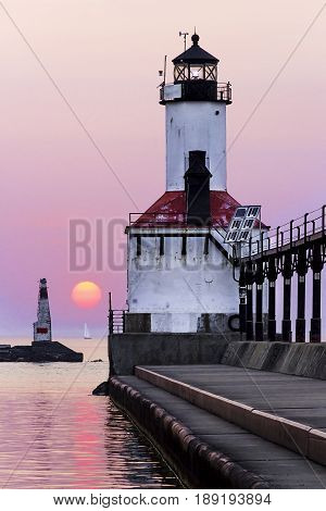 The East Pierhead Light in Michigan City Indiana with a sailboat on the horizon and setting sun.