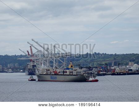 SEATTLE USA - JUNE 25 2016: Matson shipping boat towed into Seattle harbor to be unloaded by cranes in as tugboats pushes the boat.