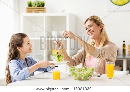 healthy eating, family and people concept - happy mother and daughter having vegetable salad for dinner at home kitchen