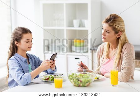 family, communication and people concept - sad mother looking at her daughter with smartphone having dinner at home