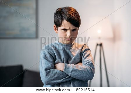Portrait Of Offended Boy With Crossed Arms Looking At Camera At Home