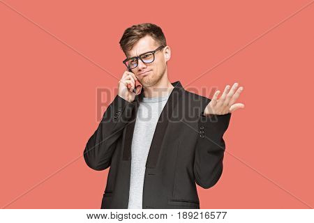 The young caucasian businessman in glasses on red studio background talking on cell phone