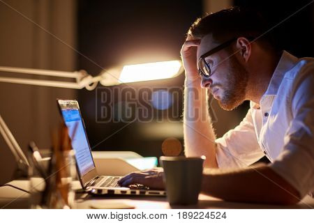 business, overwork, people, deadline and technology concept - stressed businessman in glasses with laptop computer typing at night office