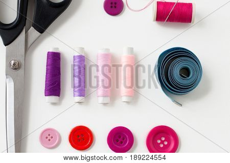 needlework and tailoring concept - scissors, sewing buttons, spools of thread and tape measure