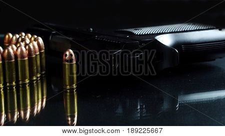 Black hand gun and bullets on the black mirror background.