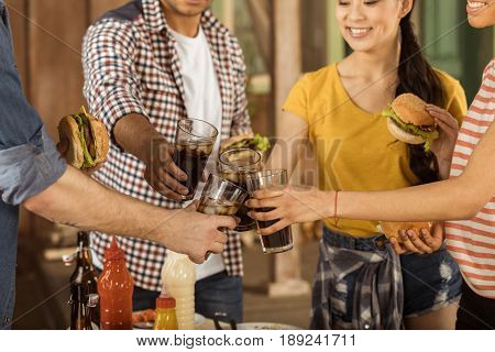 cropped shot of friends clinking with glasses of cola at picnic on patio