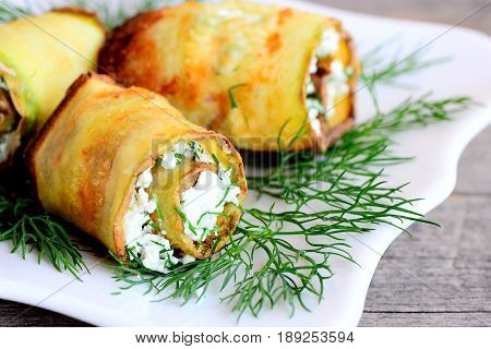 Cheese zucchini rolls. Roasted zucchini rolls stuffed with cottage cheese and herbs on a plate. Festive vegetarian appetizer recipe. Closeup