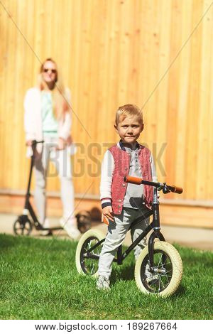 Photo of woman with boy at wooden wall on skooters in park