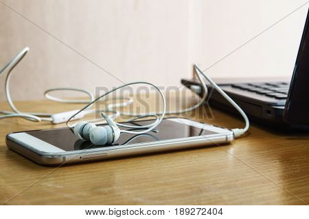 Earphones white listen to music from smartphone put on a wooden background