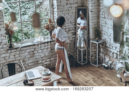 Getting dressed. Full length rear view of attractive young woman looking in the mirror while trying on her jeans