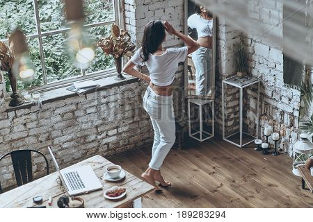 Desirable beauty. Full length rear view of attractive young woman looking in the mirror at home