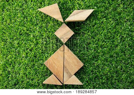 Wooden tangram puzzle in rabbit shape on artificial green grass background (Concept of Happy Easter)