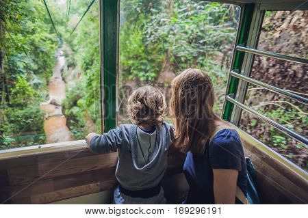 Mother And Son In Ski Lift Cabin In Summer Over The Waterfall. Passengers On A Cable Car