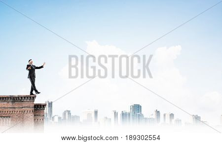 Businessman with blindfolder on eyes walking on building top