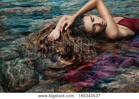 beautiful young woman in red dress laying dowm in water