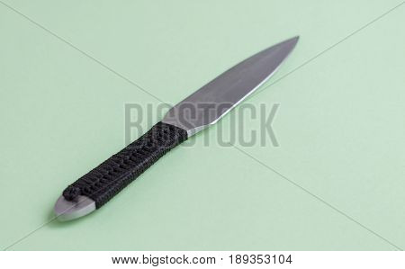 Knife for throwing with a black winding of a handle. On a light green background.