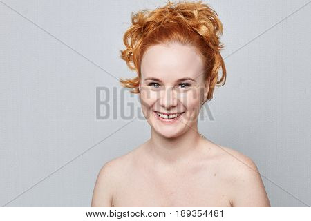Human face expressions emotions and feelings. Closeup studio portrait of beautiful young cheerful Caucasian redhead freckled woman smiling playfully at the camera on grey background wall with copy advertising space.