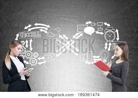Side view of two serious businesswomen one of which is reading a book while her colleague is taking notes are standing near a blackboard with infinity business sketch. Concept of never ending routine