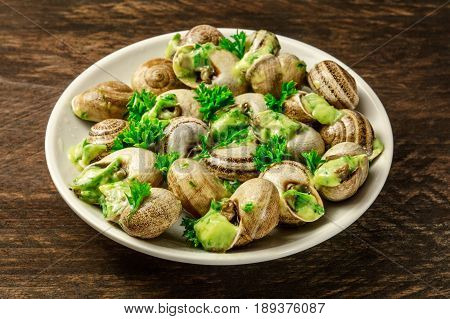 A photo of escargots a la bourguignonne, a plate of snails with the typical French green sauce of garlic and herb butter, on a rustic texture with a place for text