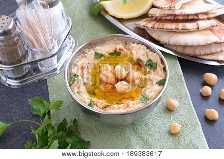 Chickpea paste with chick peas, garlic, cumin, sesami seads, olive oil, coriander in a metal bowl on a green cloth with pita bread and parsley. Traditional food. Healthy eating concept