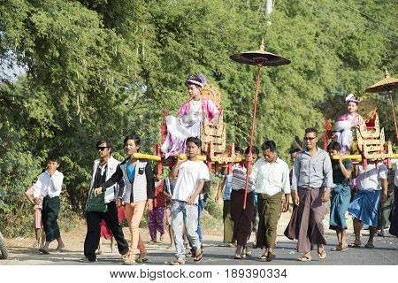 MANDALAY MYANMAR - FEB 1 2016: Boys ride on the carriage shaded with gilded umbrellas and accompanied by a procession of family members carrying offerings to a monastery in the novitiation ceremony on Feb 1 2016 in Mandalay Myanmar.