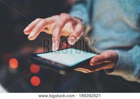 Closeup view of girl holding modern smartphone in hands.Girl typing on white touch mobile screen at night. Horizontal, blurred background, bokeh effects.Macro