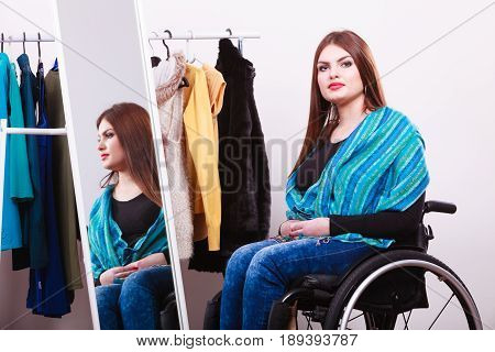 Real people disability and handicap concept. Teen girl handicapped woman sitting on wheelchair choosing clothes in wardrobe or looking for some clothes in shop