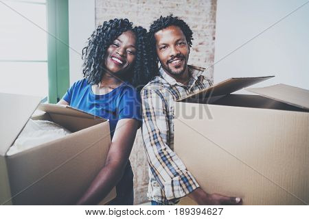 Happy young black african man and his girlfriend moving boxes into new house together and making a successful life.Cheerful family standing in empty new apartment.Horizontal.Blurred background