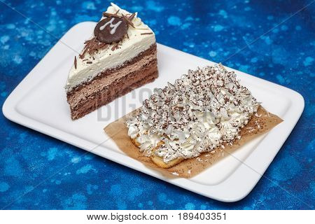 Piece of delicious mousse cake with three different kind of chocolate on white plate. Blue background