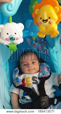 two months old baby boy in pushchair with spinning toys