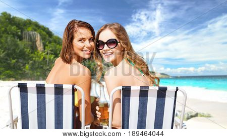 summer holidays, vacation, travel and tourism people concept - smiling young women with drinks sunbathing on folding chairs over exotic tropical beach background
