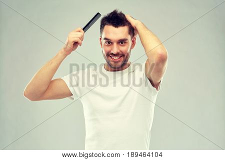 beauty, grooming and people concept - smiling young man brushing hair with comb over gray background