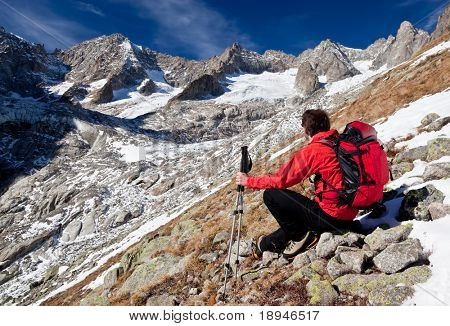 Vista posteriore di un giovane escursionista maschio osservando un panorama di alta montagna. Presa di posizione, rosso seduta