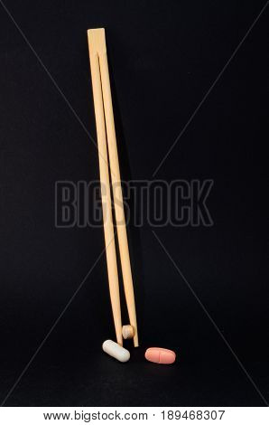 Chopsticks with tablets against a black background. Concept of health costs and drug misuse.