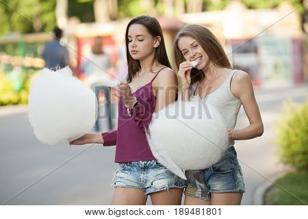 Two young women sharing cotton candyfloss at amusement park. Best friends eating cotton candy together outdoors.