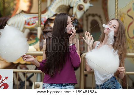 Two young women sharing cotton candyfloss at amusement park. Best friends eating cotton candy together outdoors.