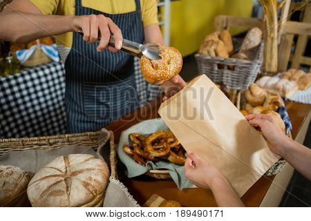 Mid section of staff packing croissant in paper bag at counter in bakery shop