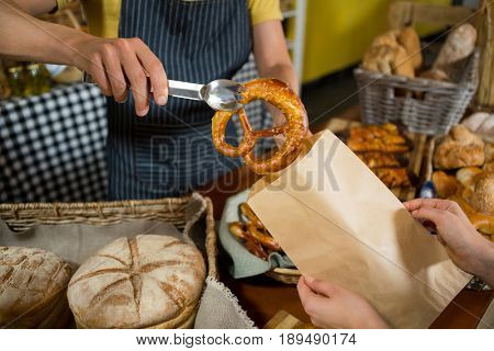 Mid section of staff packing pretzel bread in paper bag at counter in bakery shop