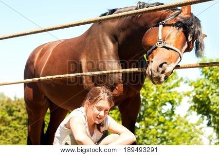 Big chestnut horse standing near his owner - cheerful young teenage girl. Multicolored vibrant outdoors horizontal summertime image.