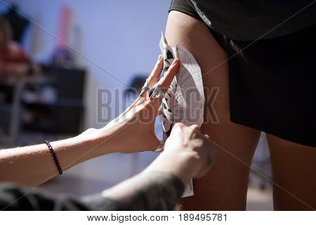 A professional tattooist is presented with sketch on the body of the girl in the Studio. Girl master and model