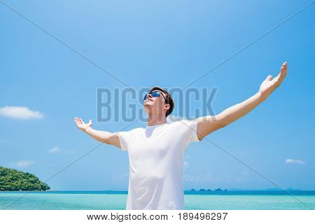 Young man raising his arms opening palms looking up in the air at the beach in summer - freedom and vacation concepts