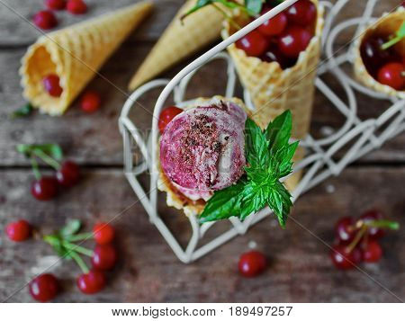 homemade ice cream cherries and chocolate in a waffle cone, fresh cherries on old wooden table - top view on the left