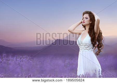 Enjoyment. Wellness. Beautiful brunette in lavender field. Carefree young woman portrait  over ridge mountains at sunset. Attractive girl with healthy long curly hair enjoying life on nature.