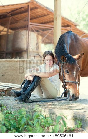 Young teenage girl equestrian sitting close to her chestnut horse. Vibrant multicolored summertime outdoors vertical image.