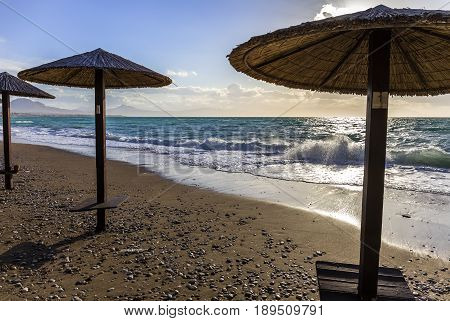 Umbreles on the sand beach with cloudy blue sky, sun and sea waves