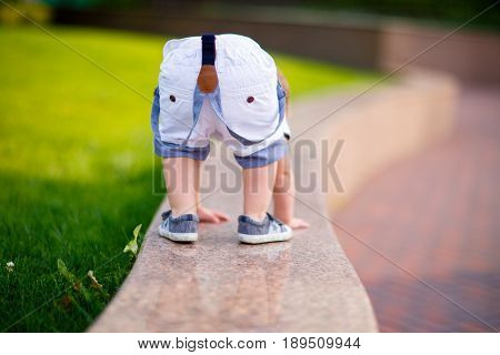 small boy in shorts on suspenders and sneakers climbed onto a shiny granite parapet in the park and turned his booty getting on all fours