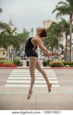 Beautiful and young ballerina leaping to left above downtown Ventura.