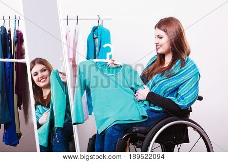 Real people disability and handicap concept. Teen girl handicapped woman sitting on wheelchair choosing clothes in wardrobe or looking for some clothes in shop