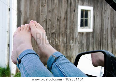 teenage girl bare feet outside open car window with old barn background